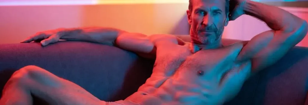 Muscular mature man posing on a bed in underwear with soft lighting