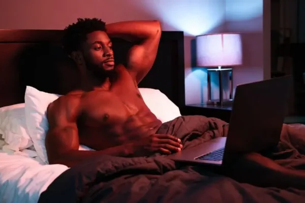 Muscular man reclining on a bed in briefs under pink and blue ambient lighting