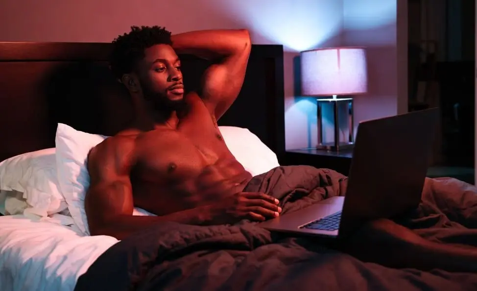 Muscular man reclining on a bed in briefs under pink and blue ambient lighting