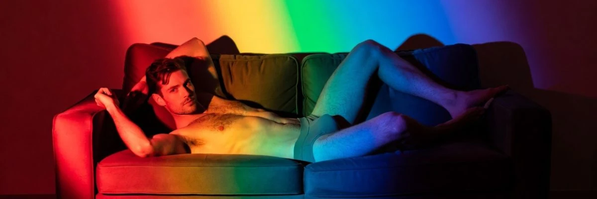 Shirtless man relaxing on a couch under colorful rainbow lighting