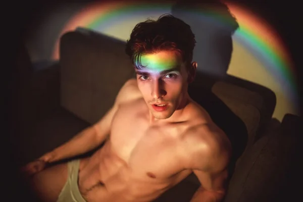 Young man with rainbow light across his face sitting on a couch